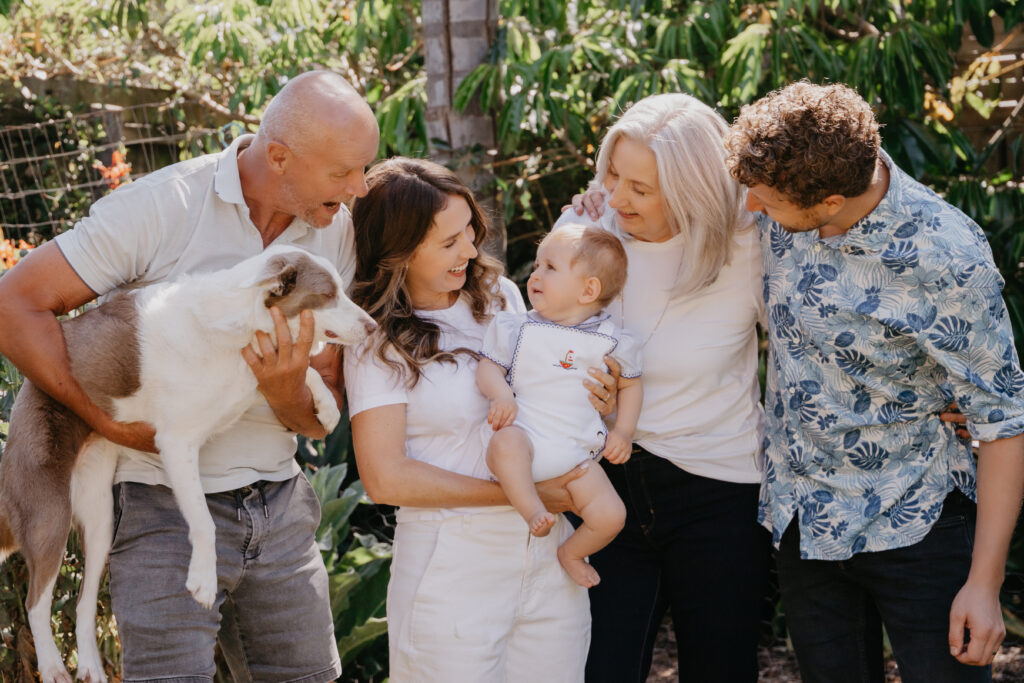 An extended family, with 9 month old baby, parents, grandparents and the pet dog photographed at home in the garden.