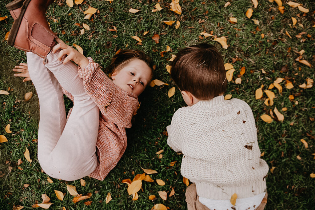 Two kids roll on the grass amongst autumn leaves