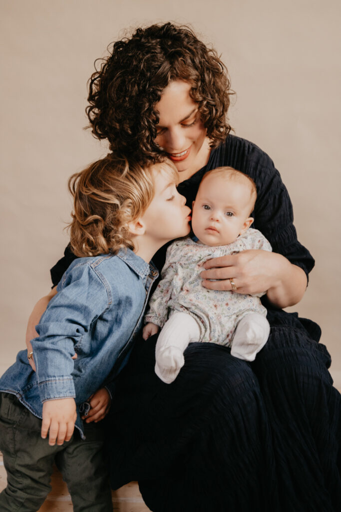 A mother with her toddler son and newborn baby girl. Natural light and simple backdrop